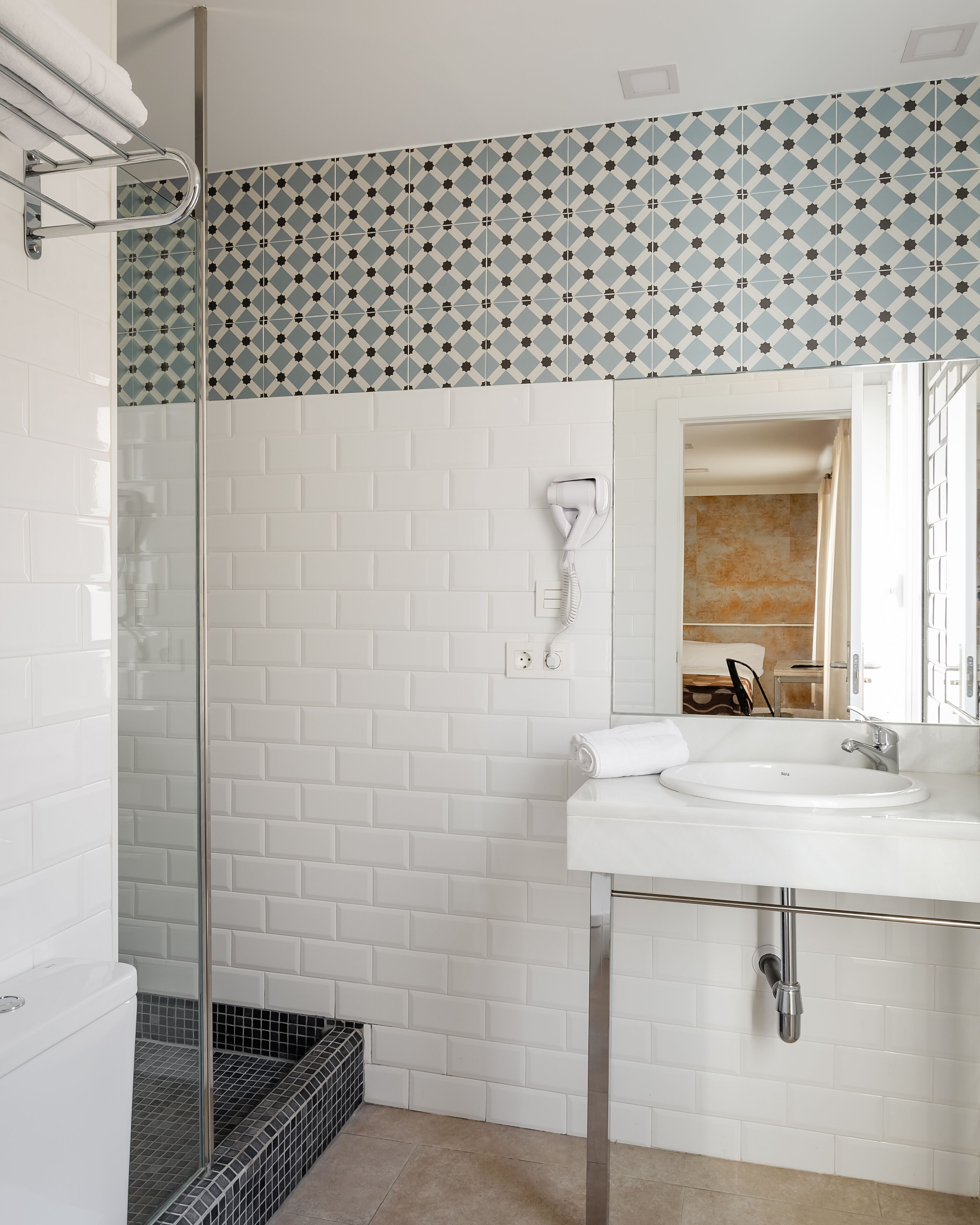 A bathroom with white subway tiles, a glass shower enclosure, a white sink with a mirror, and a towel rack.