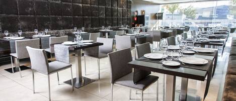 A modern restaurant with a long dining area, cushioned chairs, and neatly set tables.