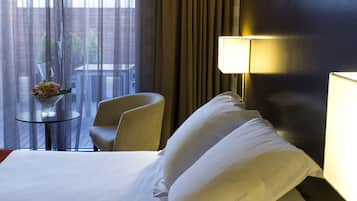 A hotel room with a bed, a chair, a small table with a vase, and two lamps.