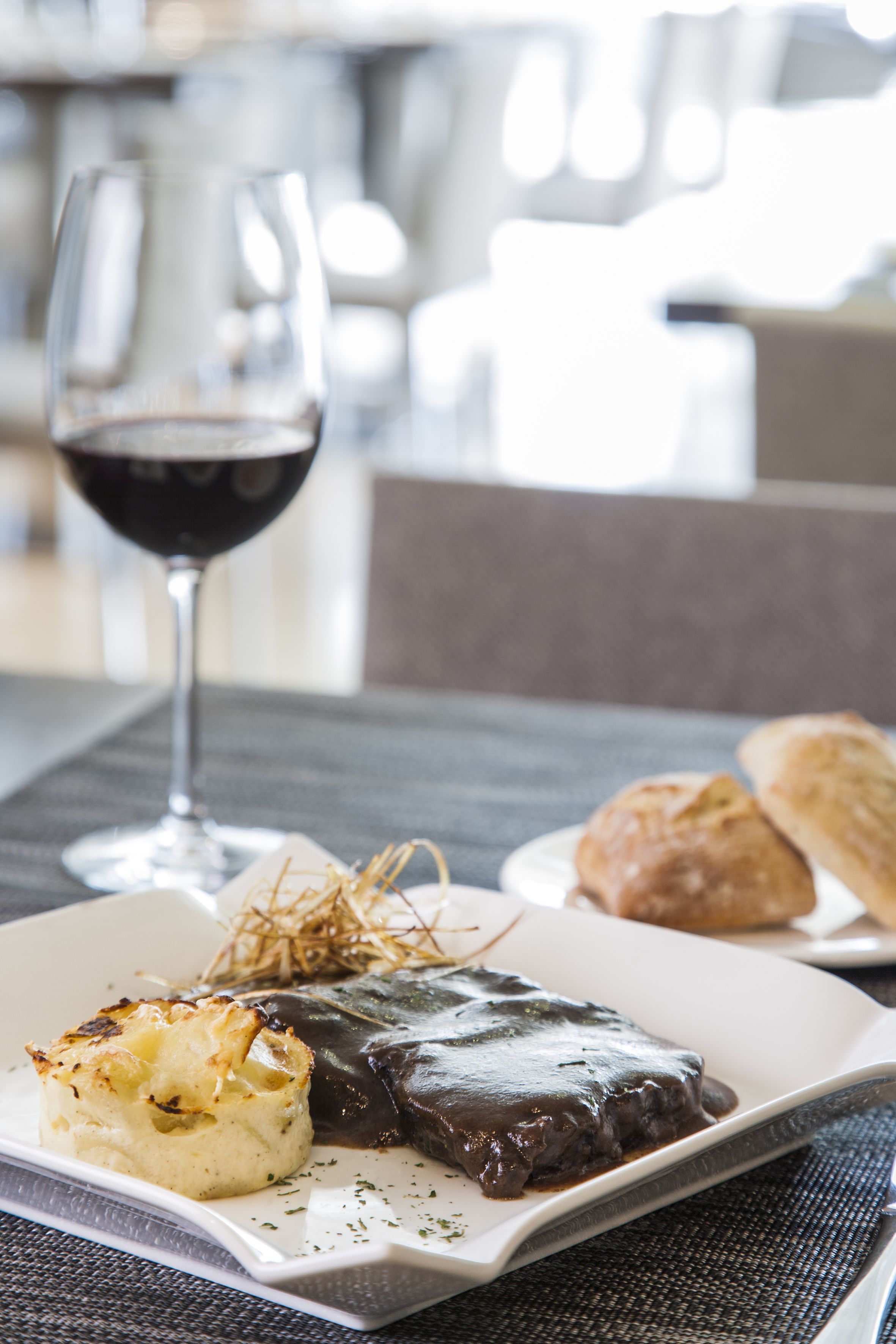 Una mesa de comedor con un plato de comida, una copa de vino tinto y una servilleta.