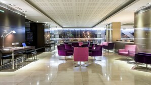 A modern lobby with a high ceiling, seating areas, and a view of the cityscape.