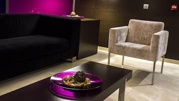 Un interior moderno con un sofá oscuro, un sillón de color claro y una mesa de centro minimalista con objetos decorativos.