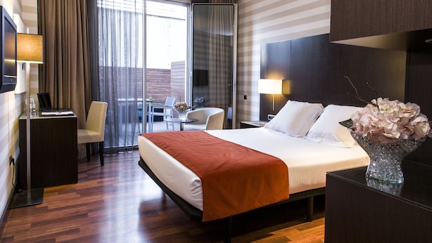 A hotel room with a large bed, a desk, a chair, and a view of the city through the window.