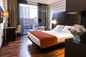 Habitación de hotel con una cama grande, un escritorio, una silla y vistas a la ciudad desde la ventana.