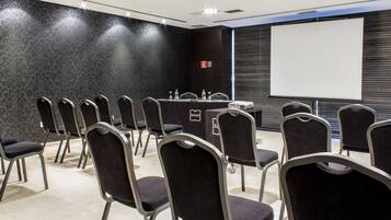 A conference room with rows of chairs, a table with a projector, and a screen.