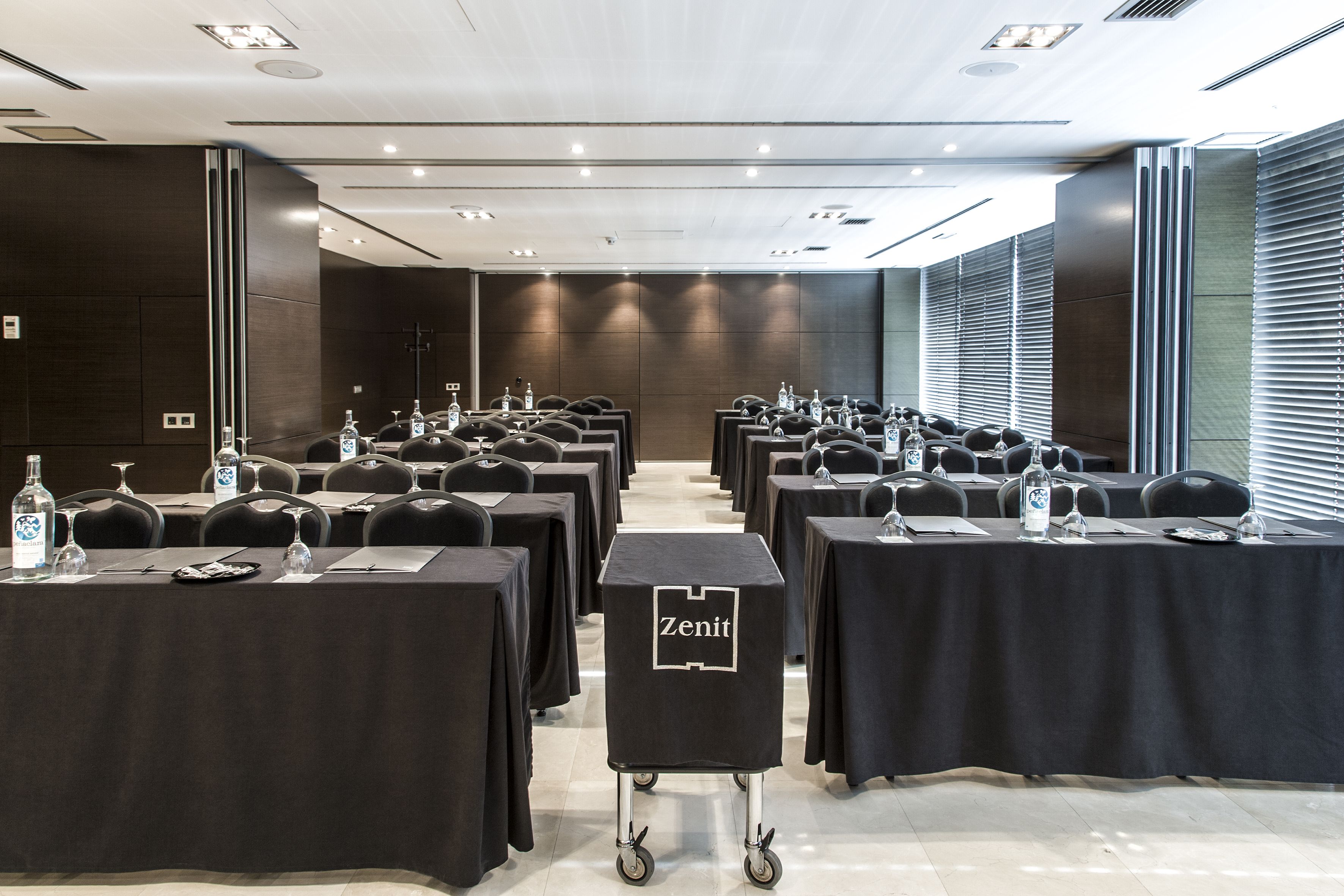 A conference room with rows of tables, each with a nameplate, water bottles, and glasses.