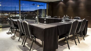 Un salón de conferencias con una mesa larga, sillas y vista a la ciudad a través de amplios ventanales.