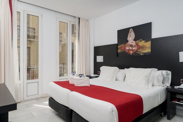 Relax in a spacious room with a large bed, nightstand, and wall-mounted artwork, plus a sliding door to a balcony with city views.