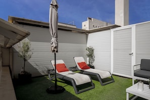 Relax in a serene outdoor space with a comfortable lounge area, featuring a table and two chairs, surrounded by lush greenery and a shaded canopy.