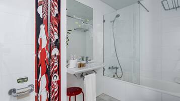 Un baño moderno con cabina de ducha de vidrio, un lavamanos blanco con espejo y un taburete rojo.