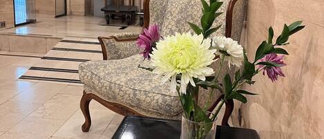 Un vestíbulo con un arreglo floral sobre una mesa, un sillón estampado y una escultura decorativa en la pared.
