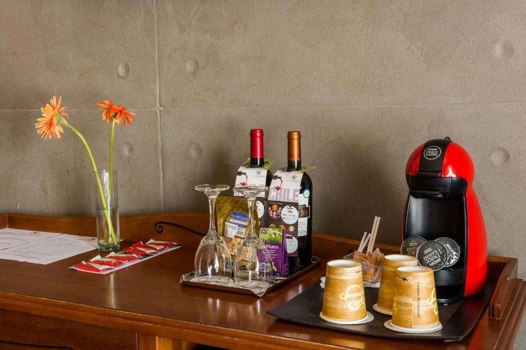 Un espace bar équipé d’une machine à café, de bouteilles de vin, de verres et d’un vase rempli de fleurs.