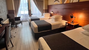 A hotel room with two beds, a desk, a chair, a lamp, and a painting on the wall.
