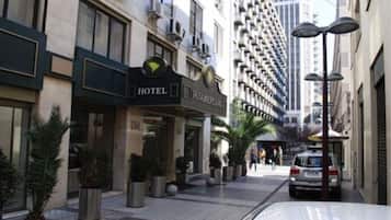 Un hotel con fachada moderna, entrada visible y zona de estacionamiento.