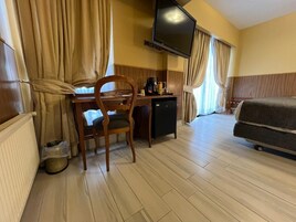 A hotel room with a wooden desk, a television, a bed, and curtains.
