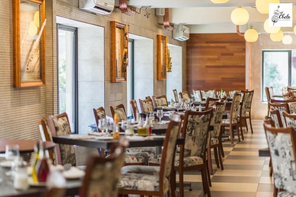 Un restaurant amb taules llargues, cadires amb dibuixos i grans finestres.