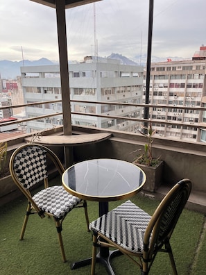 A balcony with a round table and two chairs, a potted plant, and a view of a cityscape with buildings and mountains. - Hotel Panamericano (Santiago)