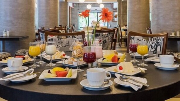 A breakfast setting with various dishes and drinks on a round table, surrounded by chairs.