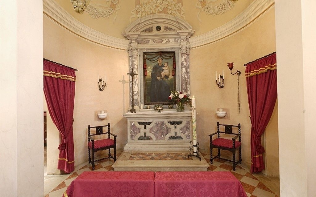 A chapel with a marble altar, two red curtains, and a bench.