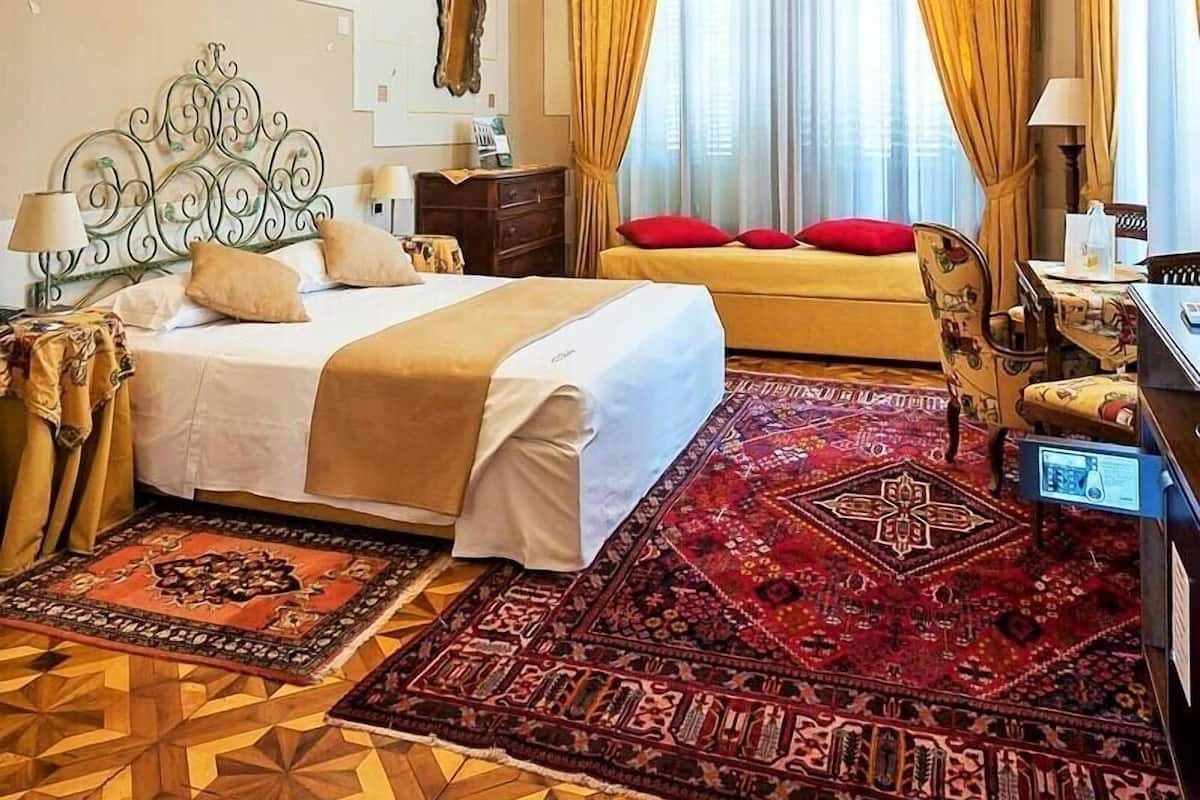 A spacious bedroom with a large bed, ornate ceiling, and a view of the outdoors through a window with yellow curtains.