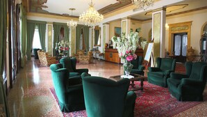 A spacious lobby with green upholstered armchairs, a large chandelier, and a red patterned carpet. - Villa Ducale (Dolo)