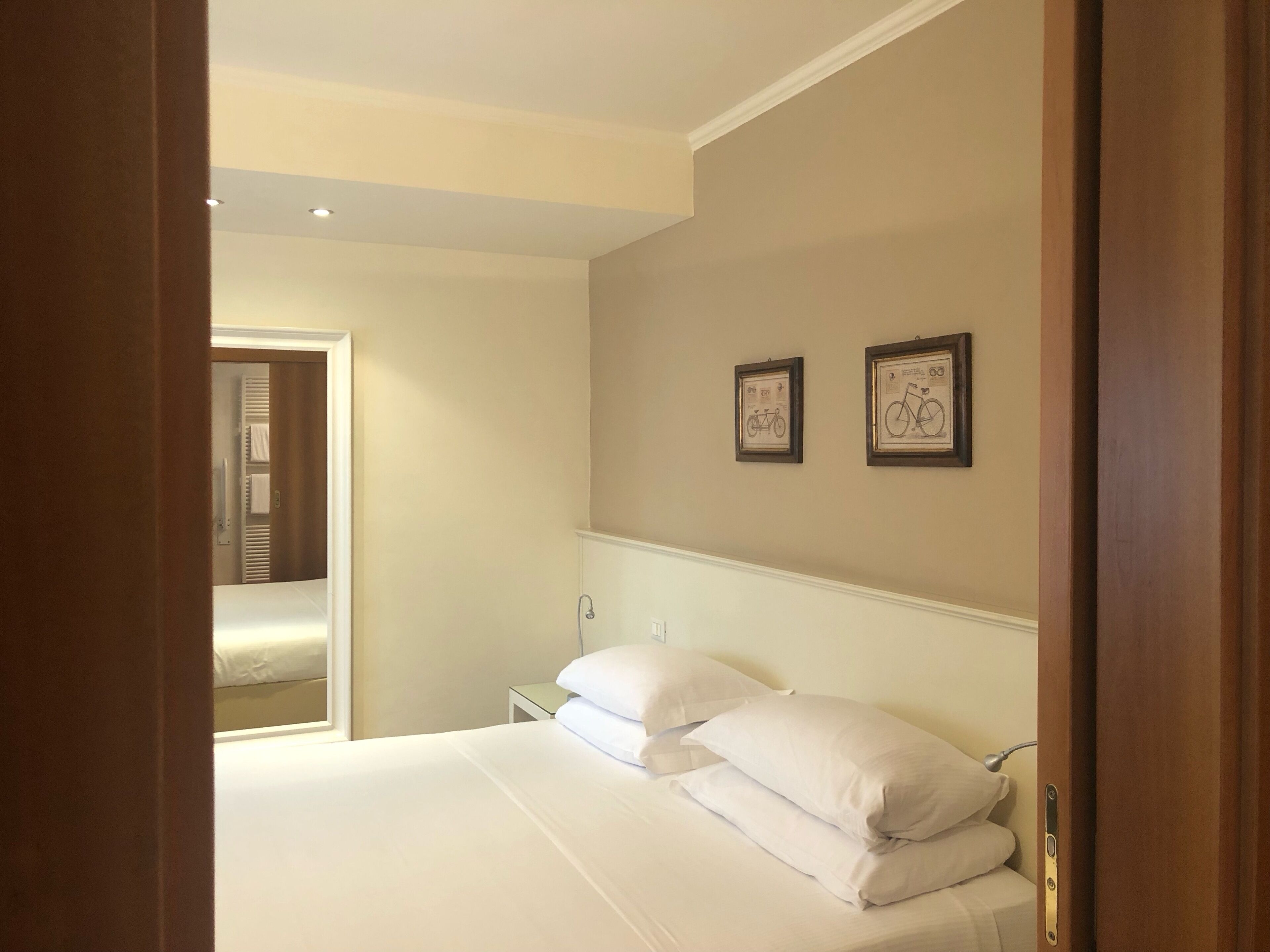 A hotel room with a bed, a nightstand, and two framed pictures on the wall.