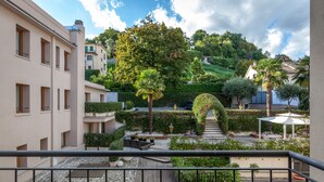 A courtyard with a wooden deck, a white umbrella, and a staircase leading to a building. - Hotel Canon D'Oro (Conegliano)