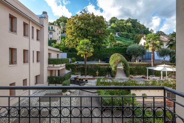 A courtyard with a wooden deck, a white umbrella, and a staircase leading to a building. - Hotel Canon D'Oro (Conegliano)