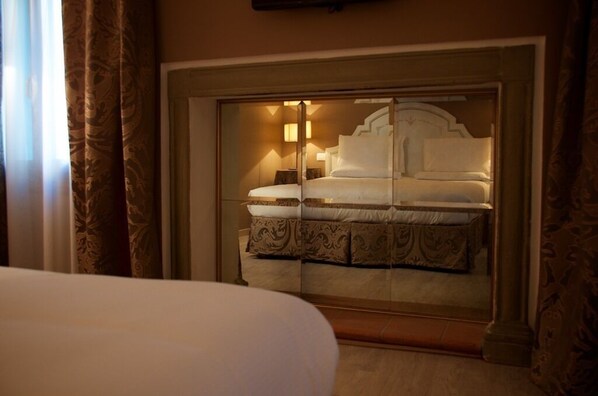 A hotel room with a large bed, a mirrored wardrobe, and a nightstand with a lamp. - Hotel Canon D'Oro (Conegliano)