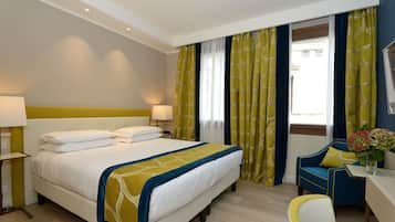 Ein Hotelzimmer mit einem großen Bett, zwei Nachttischlampen, einem Schreibtisch mit Stuhl und einem Fenster mit Vorhängen.