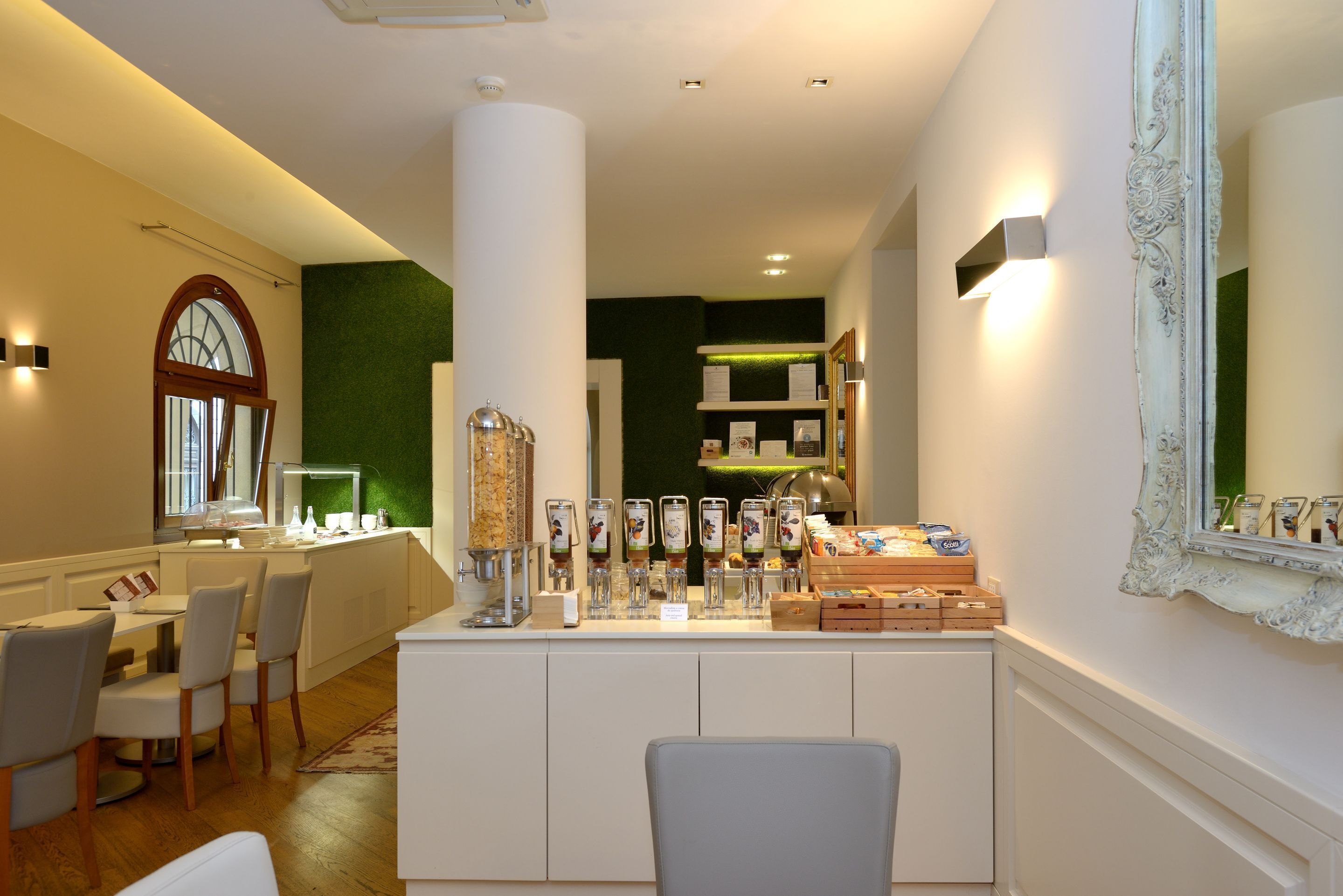 Un hall d’hôtel comprenant un comptoir d’accueil, des chaises, un grand miroir et un mur vert.