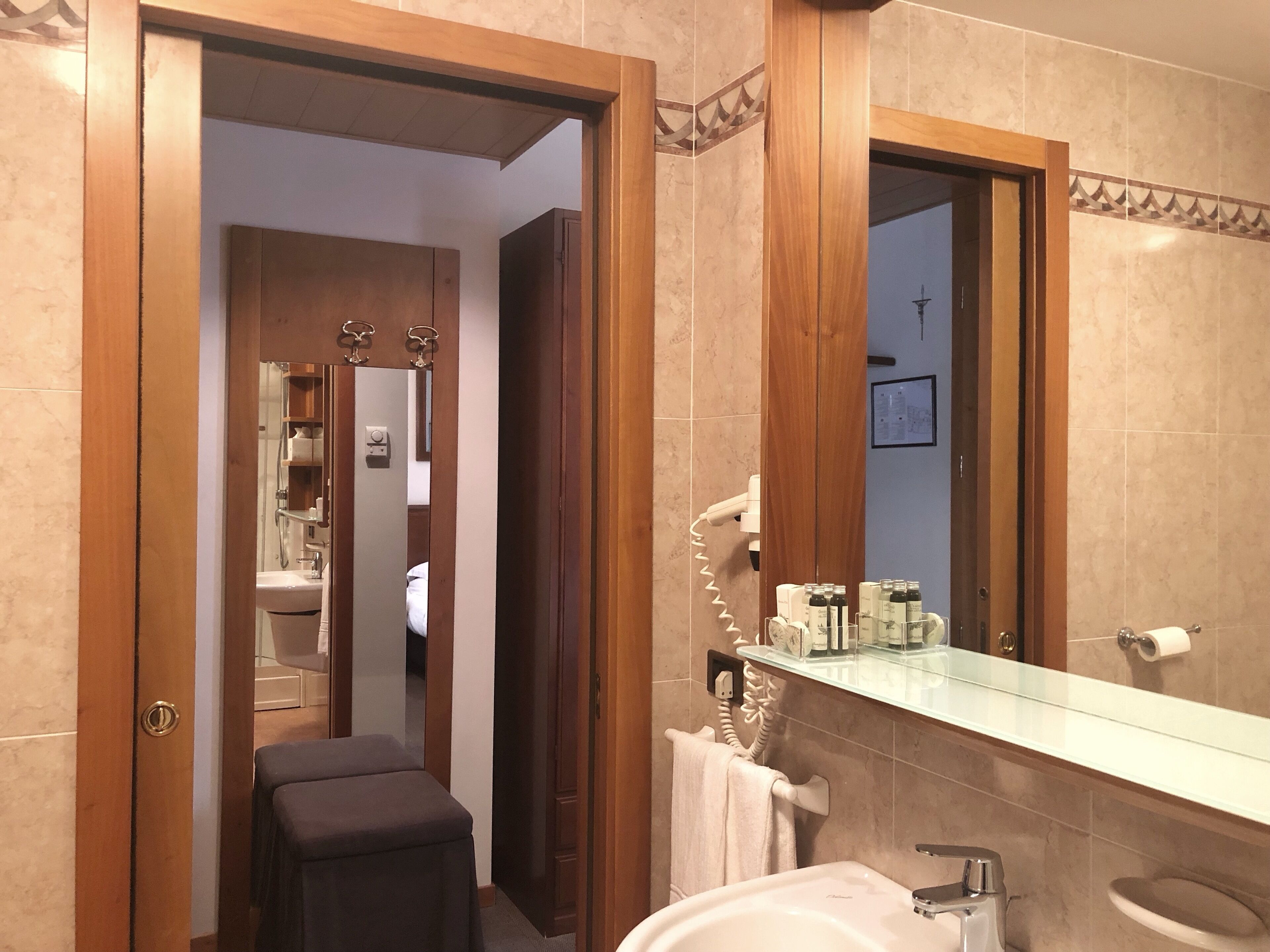 A bathroom with a mirror, sink, and towel rack. There is a door leading to a bedroom.