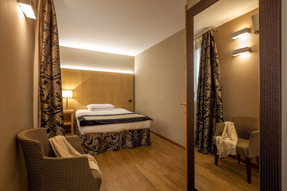 Une chambre d’hôtel avec un lit, une chaise, une petite table et un miroir.