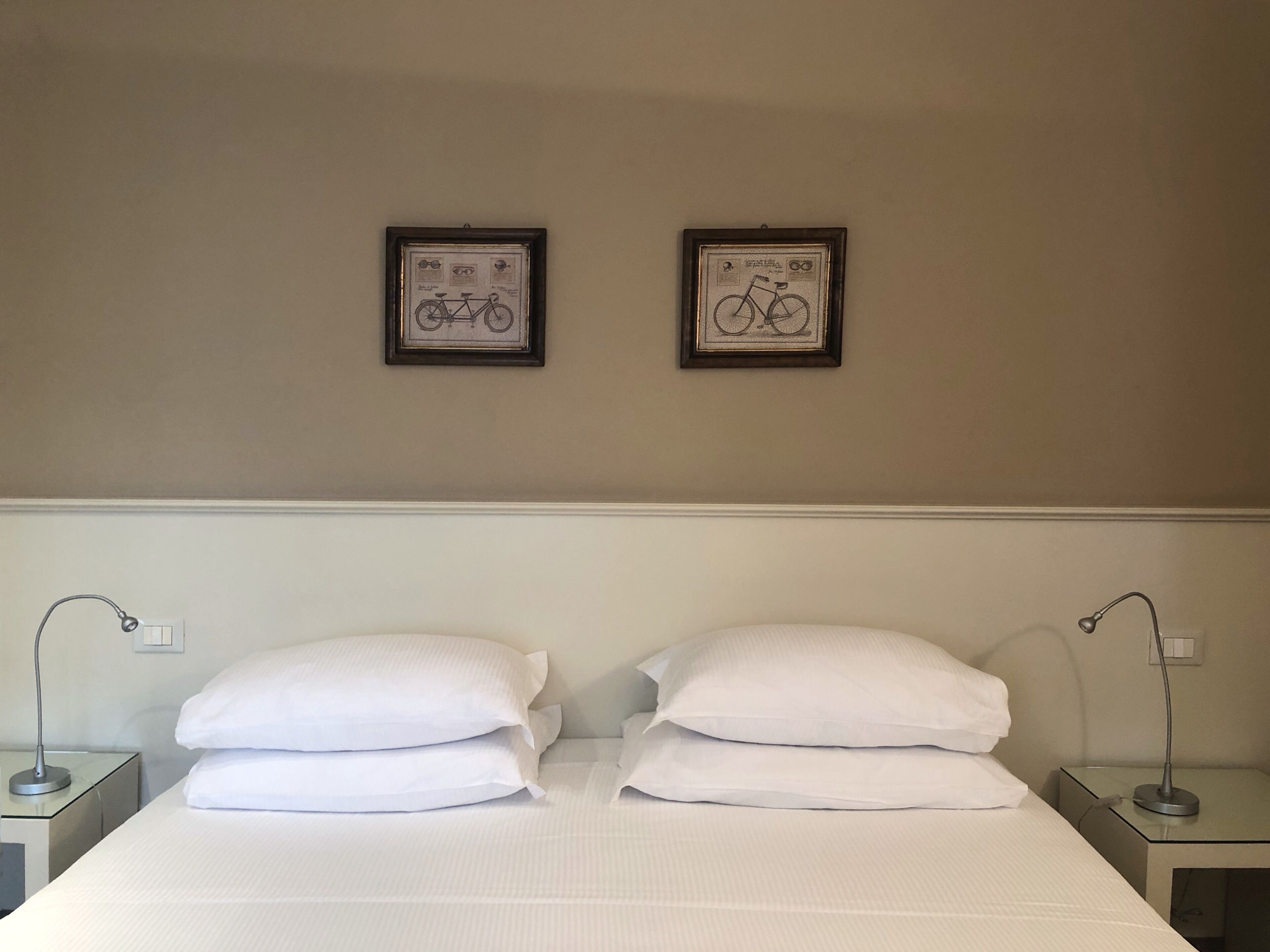 A hotel room with a large bed, two white pillows, two nightstands with lamps, and two framed pictures on the wall.