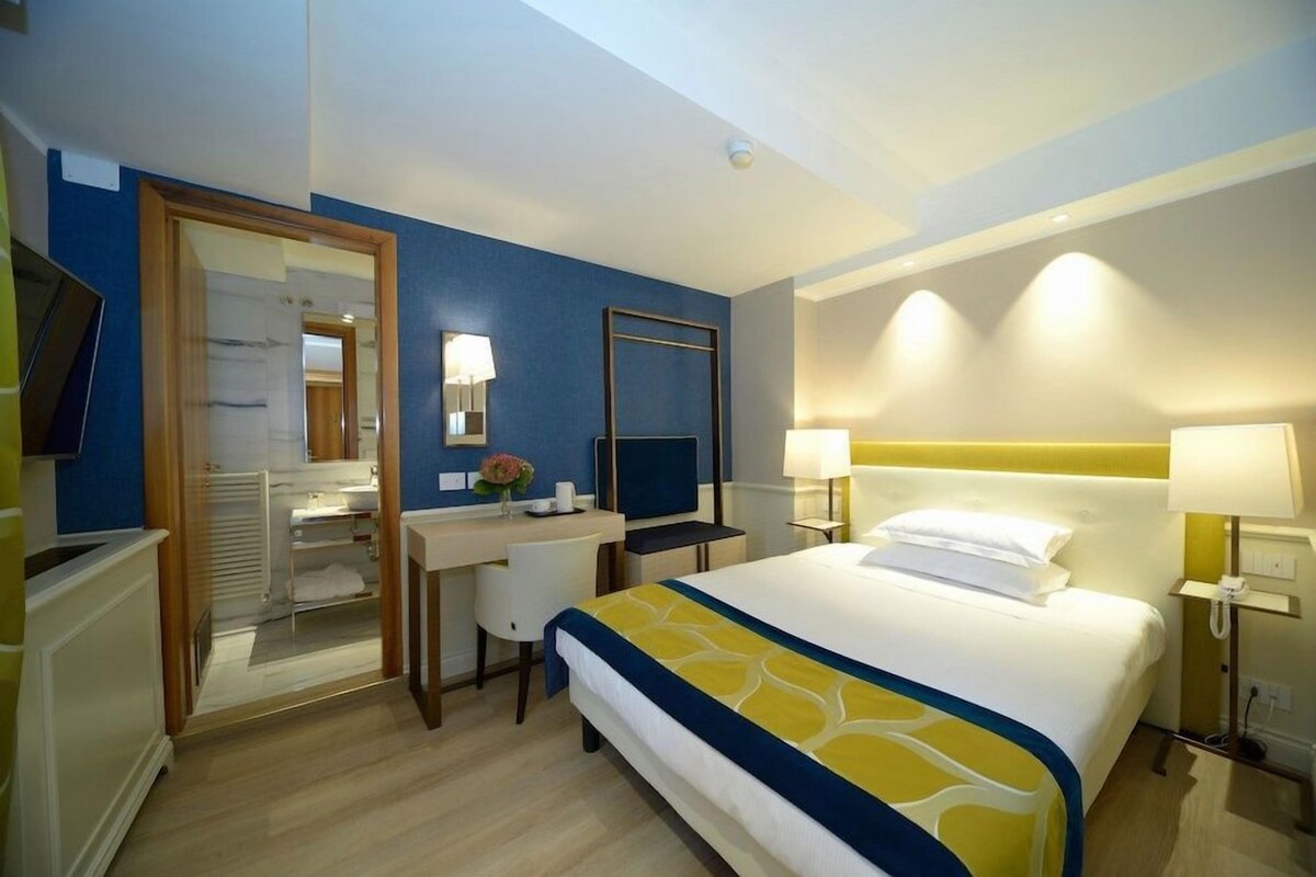 A hotel room with a bed, desk, and a mirror.