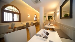 A restaurant with white tables and chairs, large windows, and a mirror on the wall. - Hotel Canon D'Oro (Conegliano)