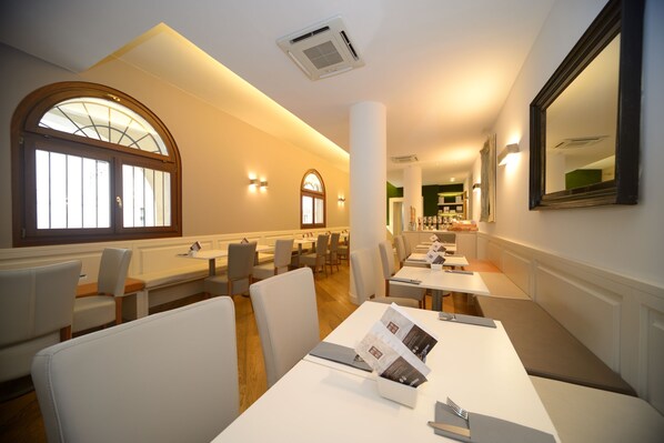A restaurant with white tables and chairs, large windows, and a mirror on the wall. - Hotel Canon D'Oro (Conegliano)