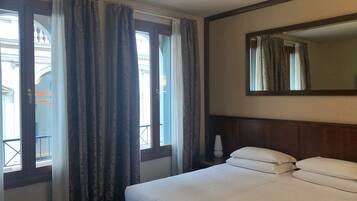 Una habitación de hotel con cama, mesita de noche, espejo y ventana con cortinas.