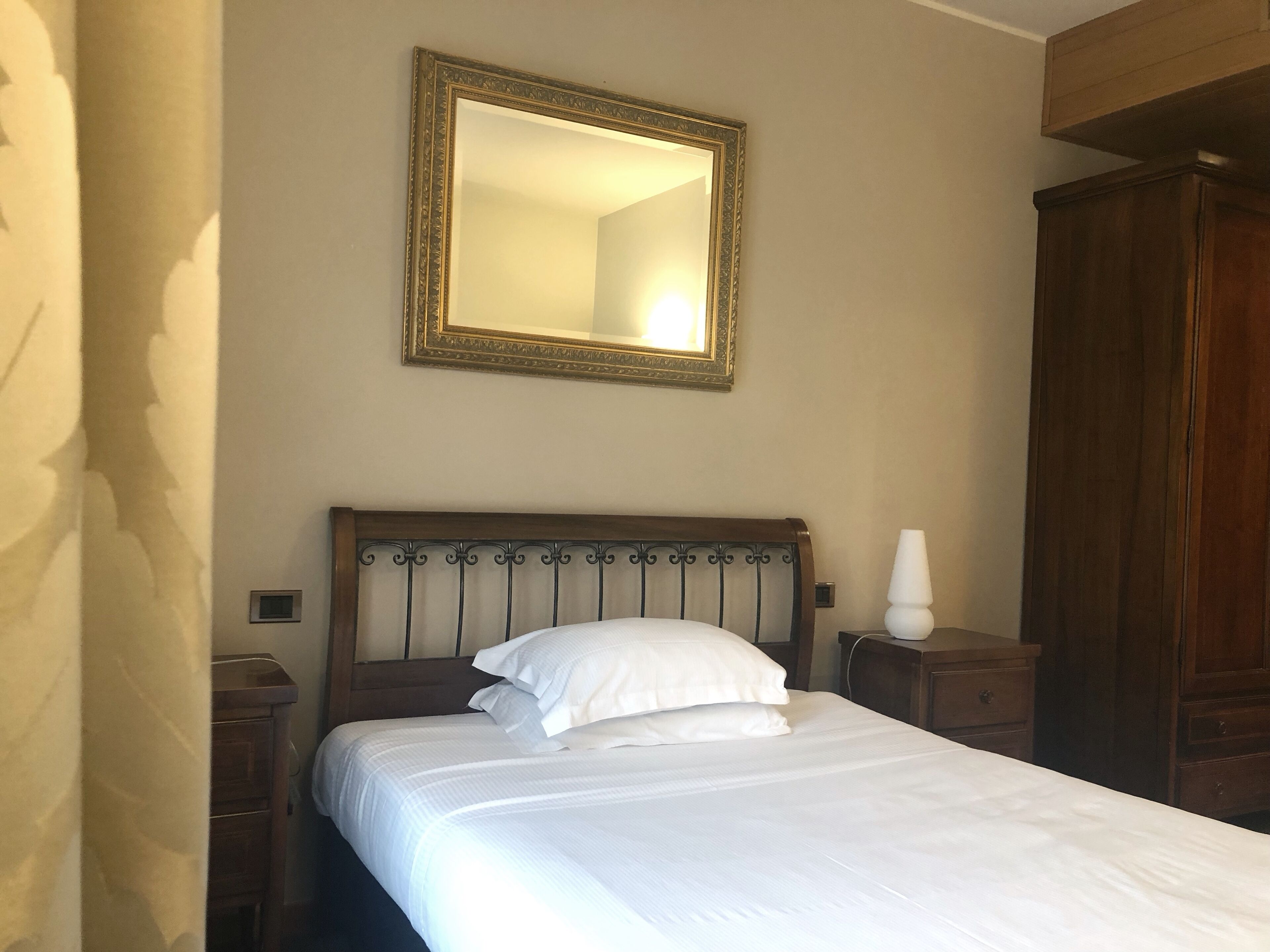 Un lit bien fait, avec du linge de lit blanc, une tête de lit en bois et un grand miroir au-dessus.