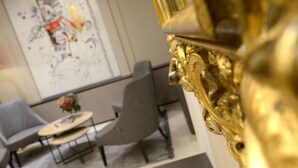 A modern interior with a golden ornate object, two grey chairs, a small round table with a vase, and a large abstract painting on the wall. - Hotel Canon D'Oro (Conegliano)