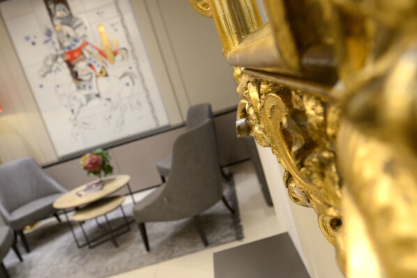 A modern interior with a golden ornate object, two grey chairs, a small round table with a vase, and a large abstract painting on the wall. - Hotel Canon D'Oro (Conegliano)
