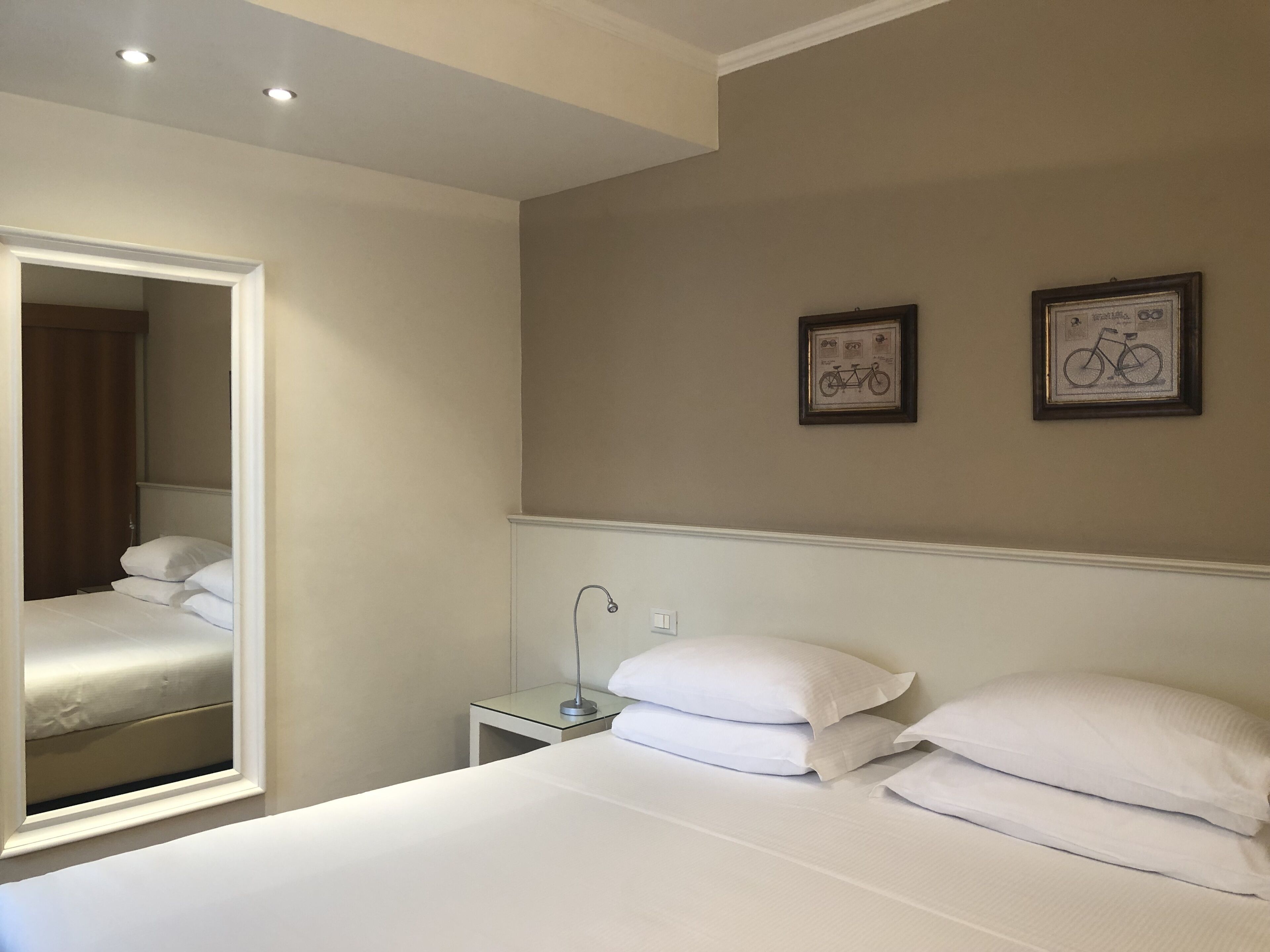 A hotel room with a large bed, a nightstand, a mirror, and two framed pictures on the wall.