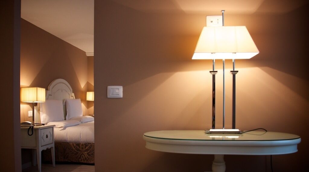 A hotel room with a bed, bedside lamps, a nightstand, and a wall-mounted lamp.