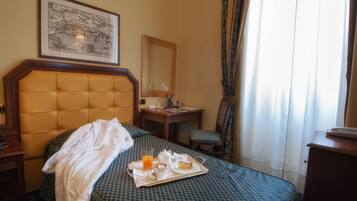 Una camera d'albergo con un letto, un comodino, una scrivania, una sedia, una finestra con tende e un quadro appeso al muro.