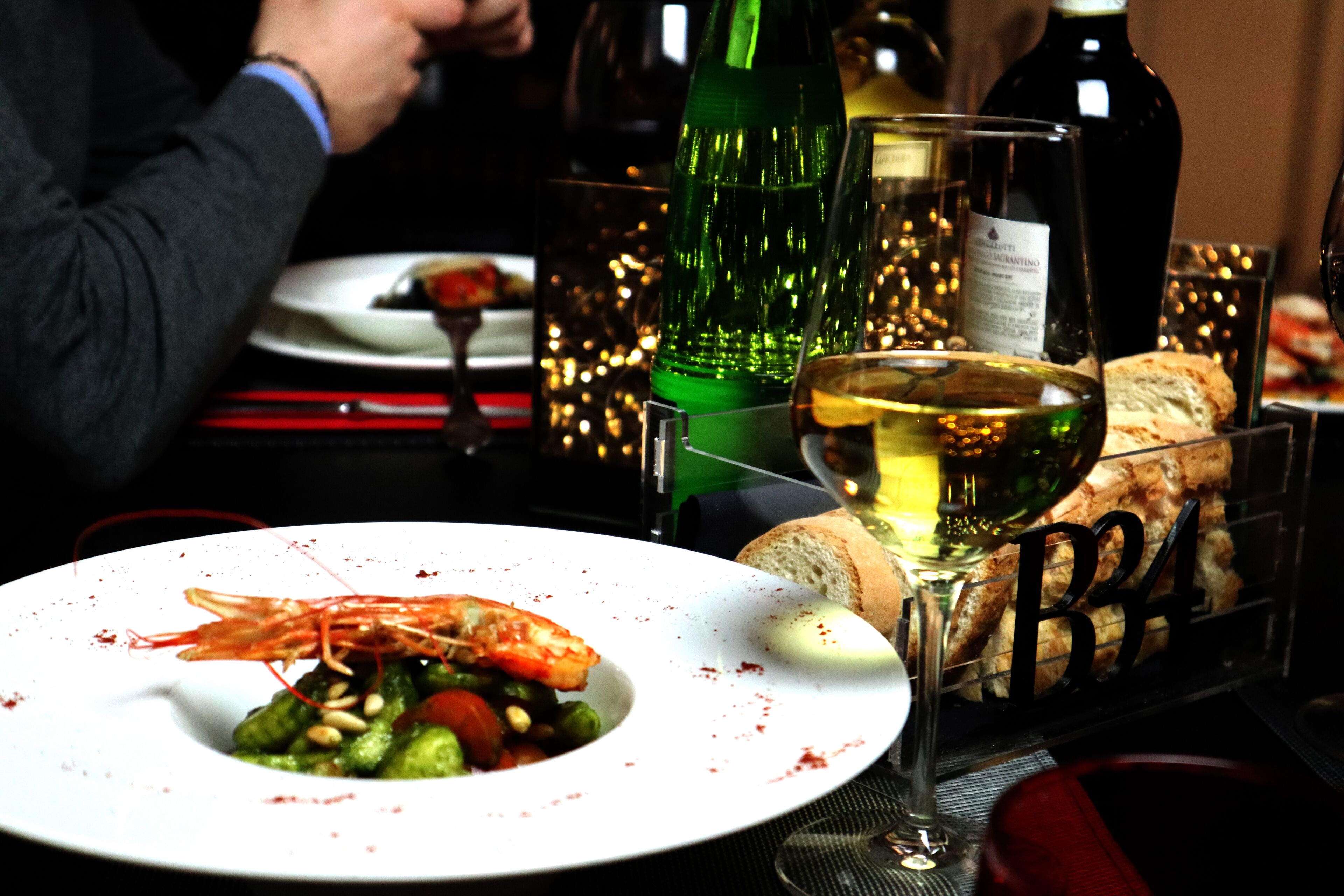 A dining table with a plate of food, a glass of wine, and several bottles of wine.