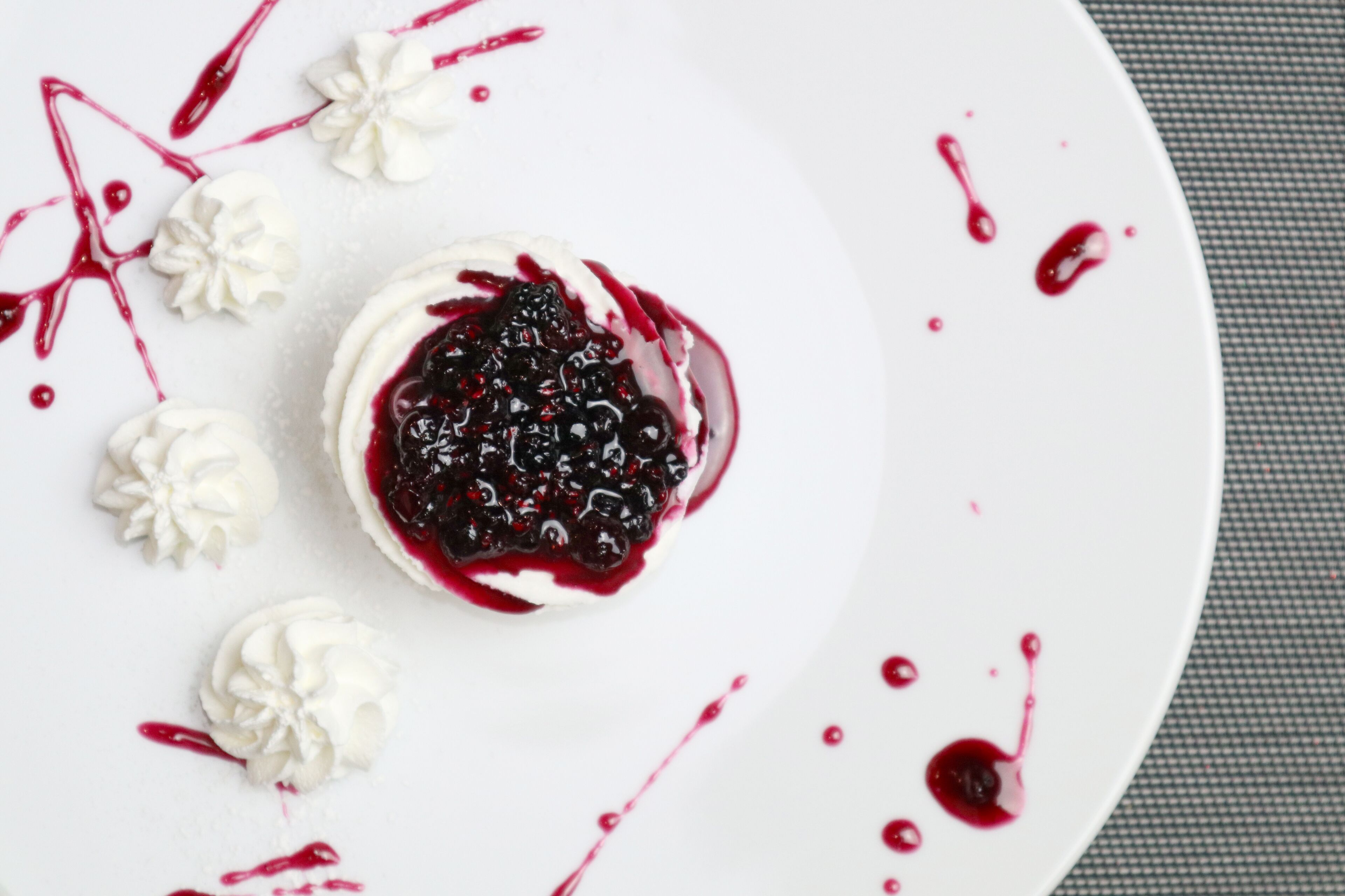Un postre con crema batida y compota de frutos rojos sobre un plato blanco.