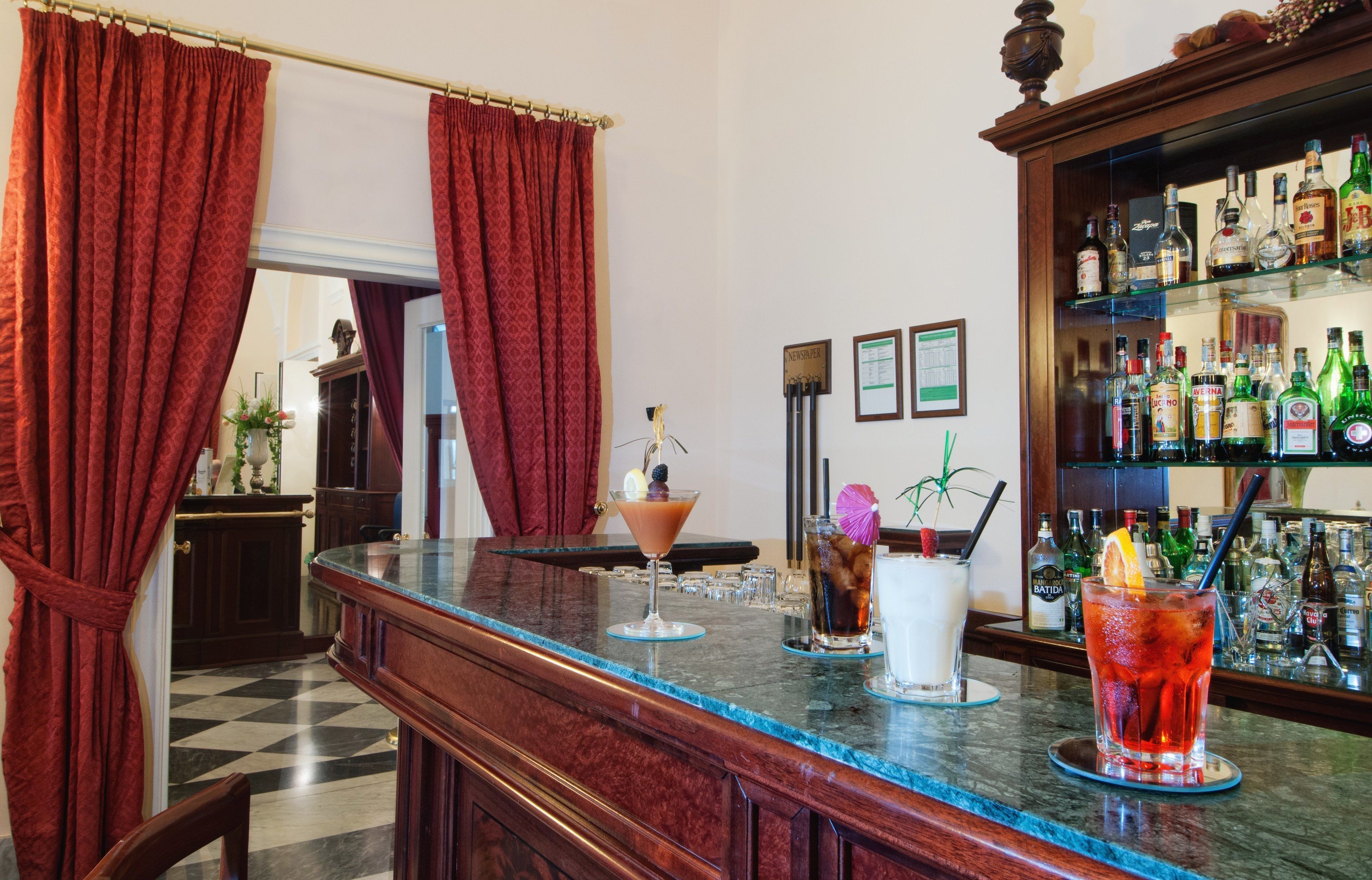 Un espace bar doté d’un comptoir en marbre, de rideaux rouges et d’une variété de bouteilles d’alcool.