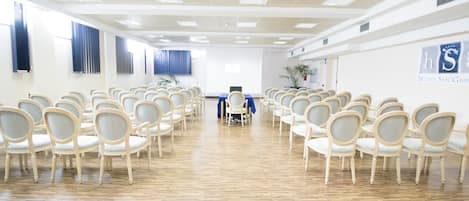 Une salle de conférence d’hôtel avec des rangées de chaises, un pupitre et une grande fenêtre.