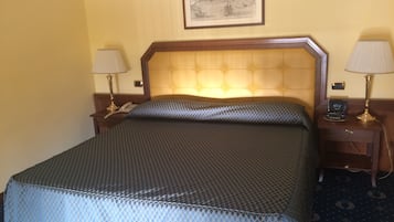 A hotel room with a large bed, two bedside tables with lamps, a clock, and a framed picture on the wall.