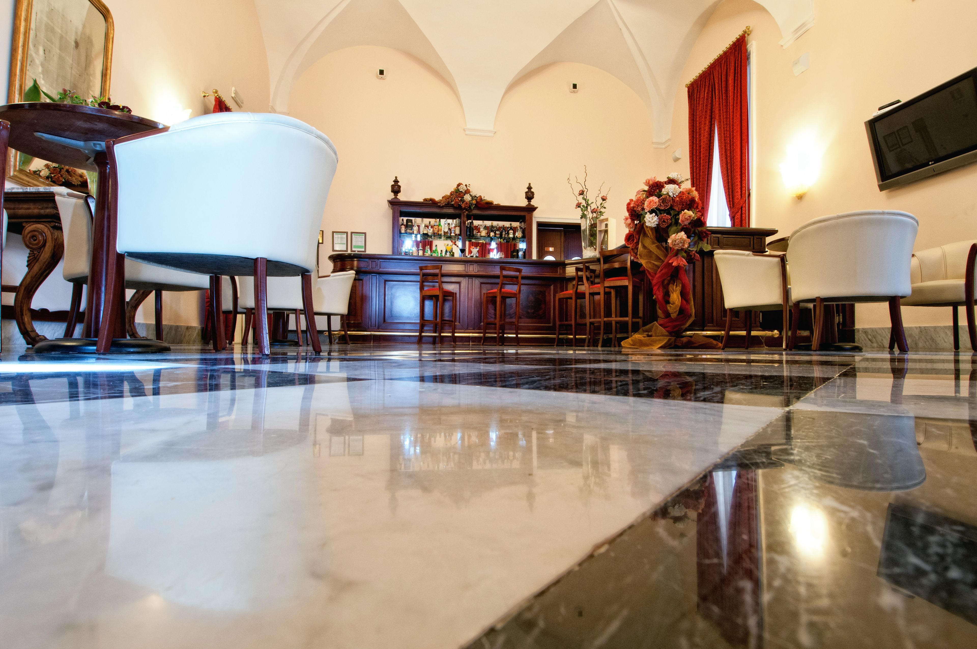 A bar area with a marble floor, wooden chairs, and a bar counter with bottles.